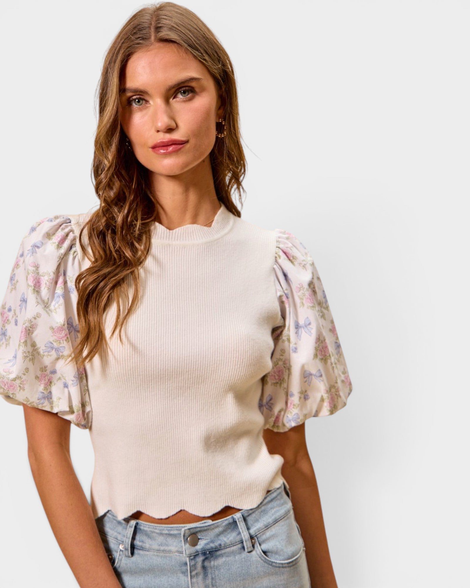 Woman wearing a cream top with floral sleeves and jeans on a white background