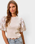 Woman wearing a cream top with floral sleeves and jeans on a white background