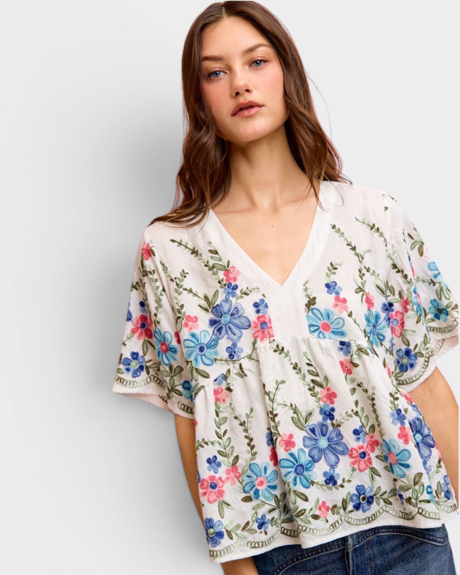 Woman wearing a floral embroidered top against a plain background