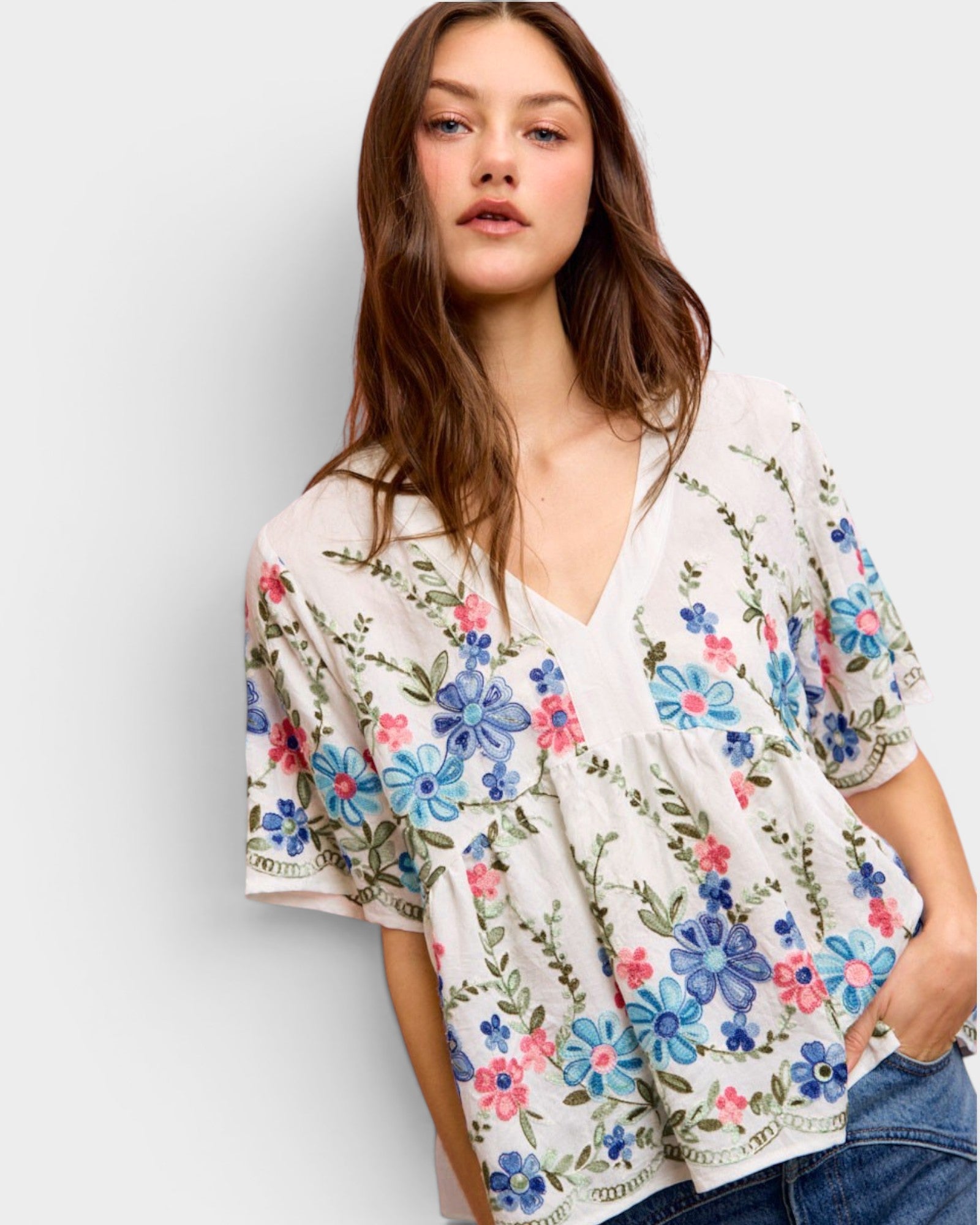 Woman wearing a floral embroidered top against a plain background