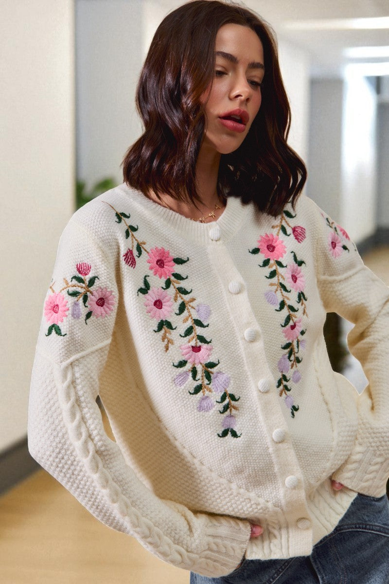 Woman wearing a cream-colored sweater with floral embroidery in an indoor setting