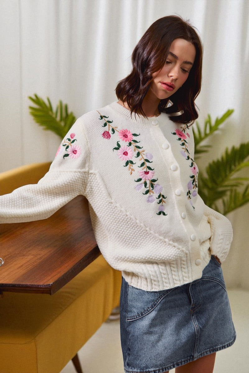 Woman wearing a white sweater with floral embroidery in a home setting