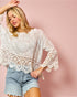 Woman wearing a white lace blouse and denim shorts against a pink background