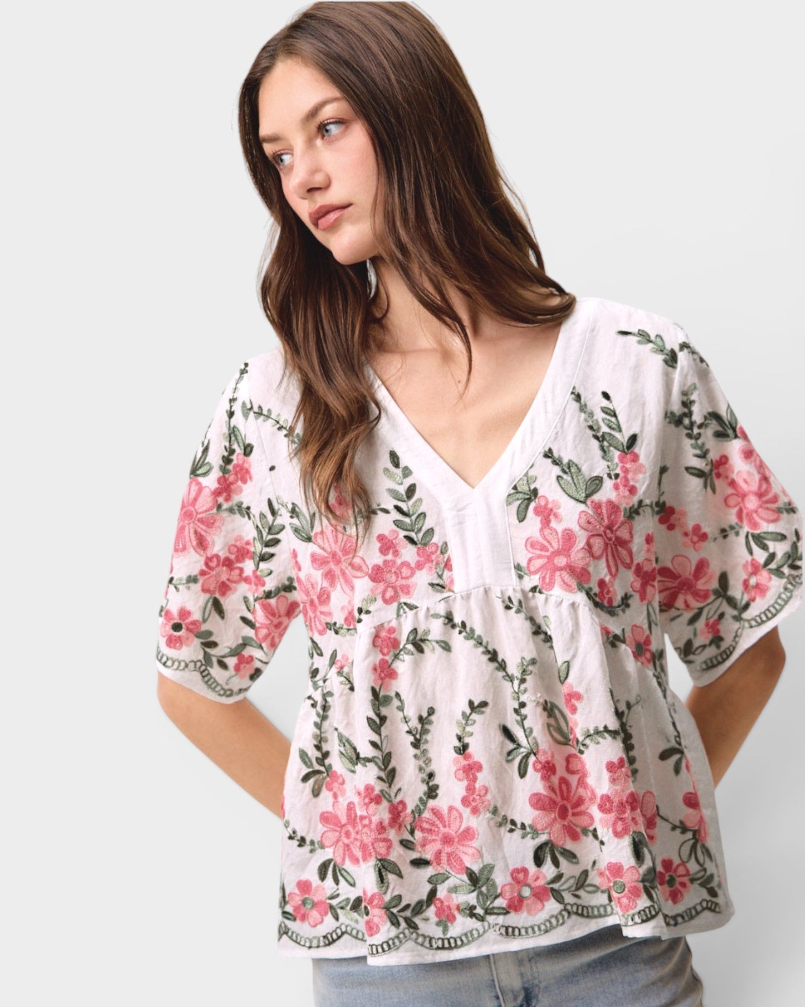 Woman wearing a white blouse with pink floral patterns on a plain background