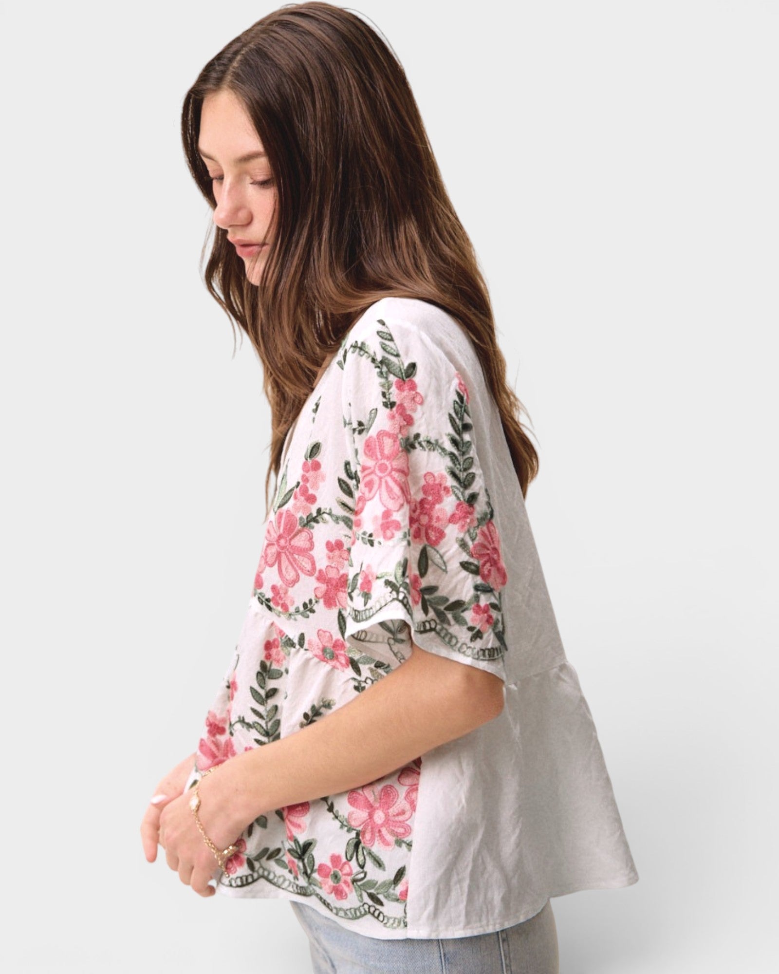 Woman wearing a white kimono-style top with pink floral patterns on a plain background