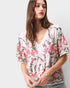Woman wearing a floral blouse with pink flowers on a plain background