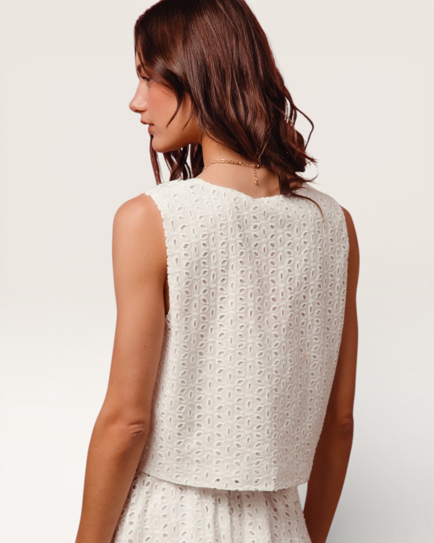 Woman wearing a white sleeveless top with a subtle pattern on a plain background