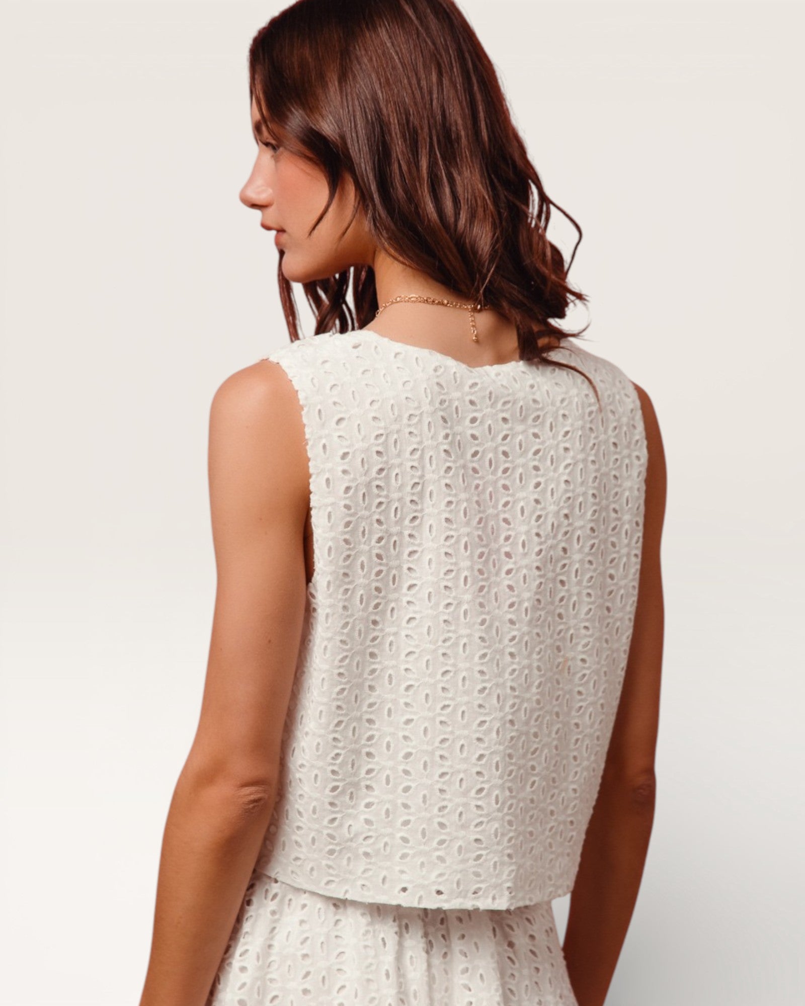 Woman wearing a white sleeveless top with a subtle pattern on a plain background