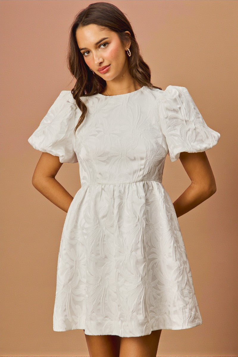 Woman wearing a white dress with puffed sleeves against a beige background