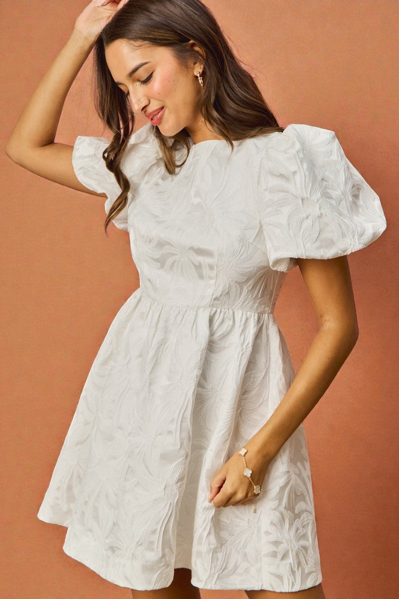 Woman wearing a white dress with puffed sleeves against a brown background