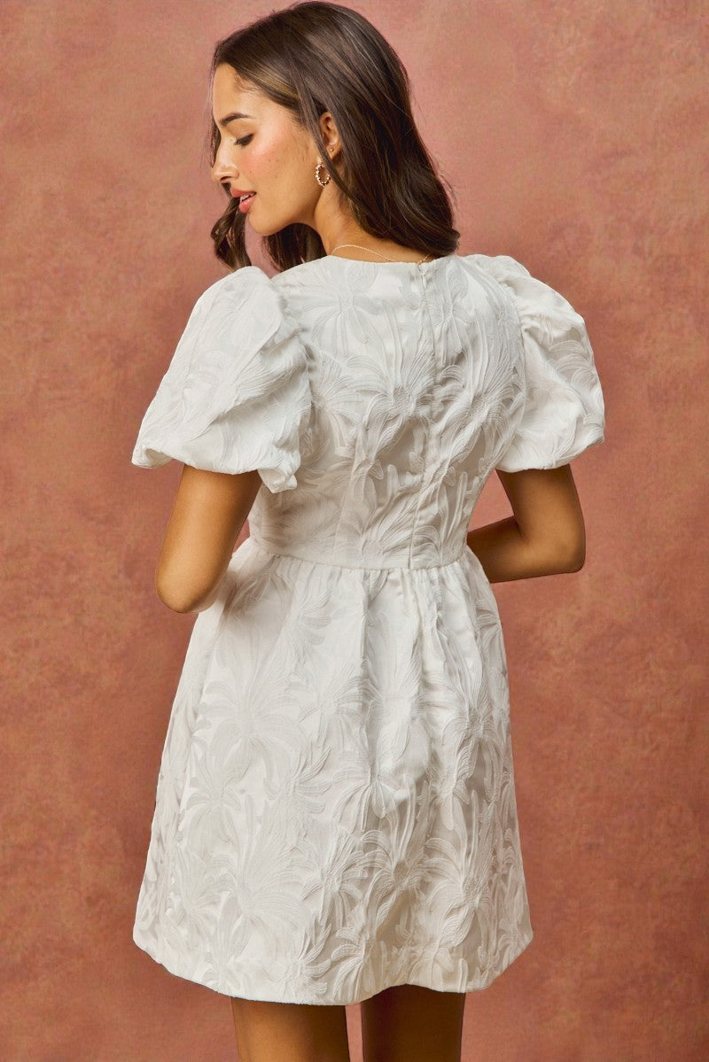 Woman wearing a white dress with puffed sleeves against a brown background