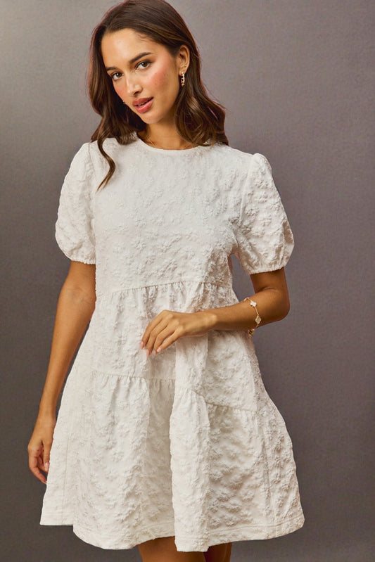 Woman wearing a light gray dress with puff sleeves against a gray background