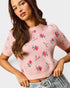 Woman wearing a pink floral embroidered sweater against a plain background