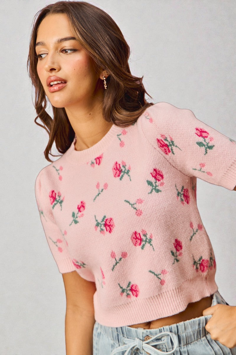 Woman wearing a pink sweater with floral patterns against a gray background