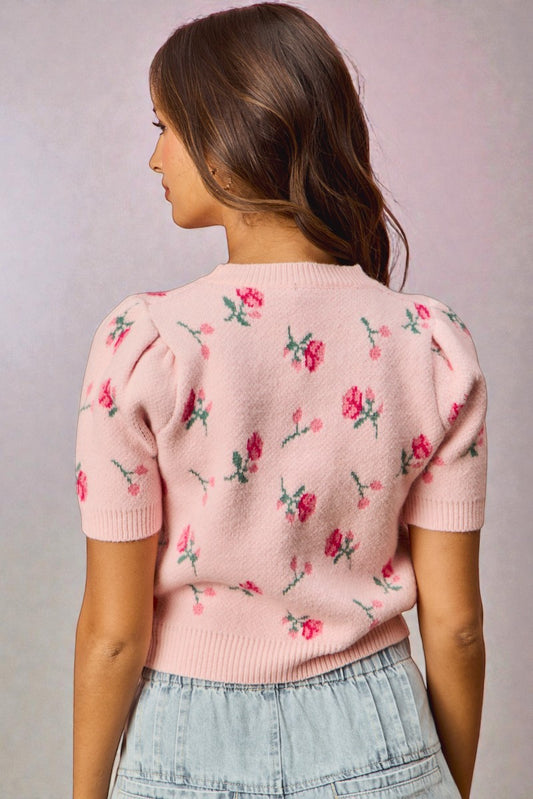 Woman wearing a pink floral-patterned sweater against a plain background