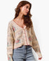 A woman wearing a cream-colored knit cardigan with a pink and green floral pattern, paired with light blue jeans, against a plain white background.