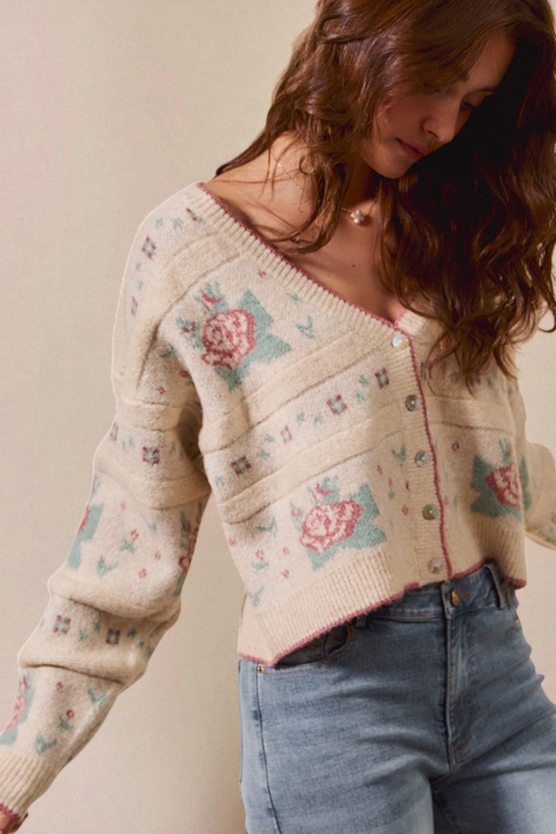 Woman wearing a patterned cardigan with floral designs against a plain background