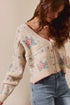 Woman wearing a patterned cardigan with floral designs against a plain background