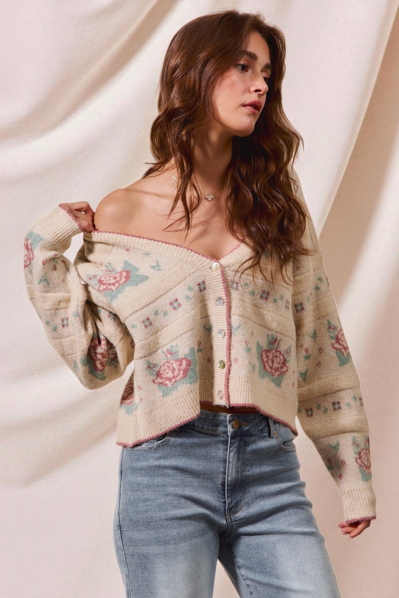 Woman wearing a floral patterned cardigan over a pink top with light blue jeans against a beige background