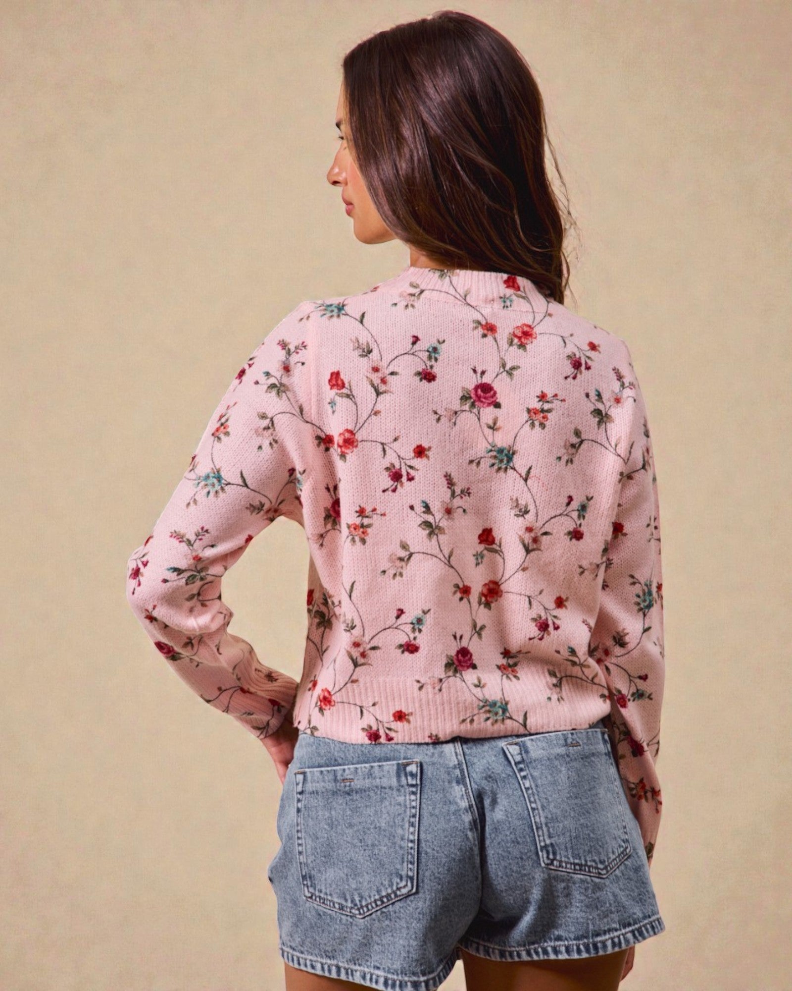 Woman wearing a pink floral sweater and denim shorts against a beige background
