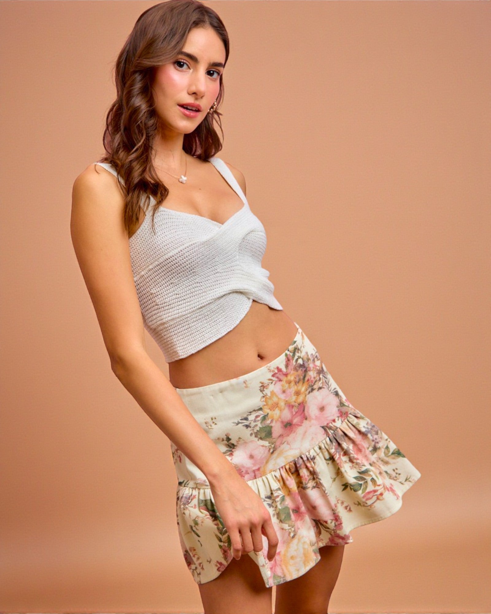 Woman wearing a white crop top and floral skirt on a beige background