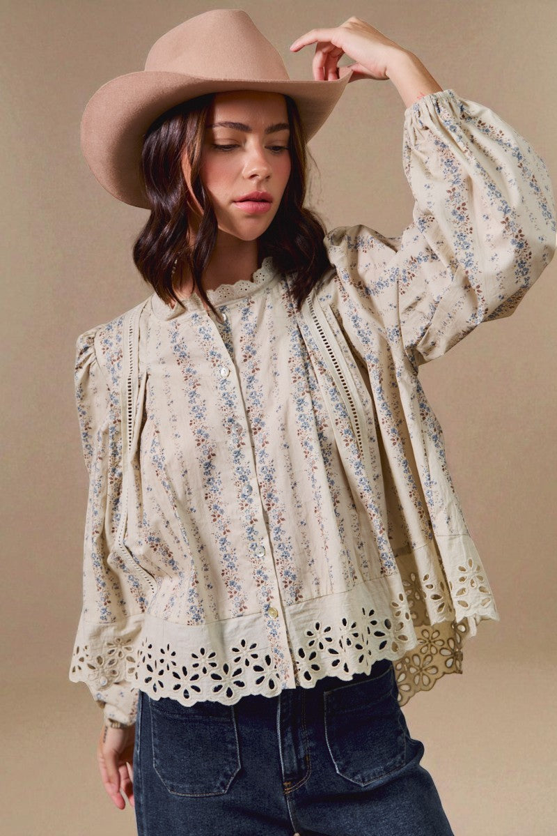 Woman wearing a floral blouse with lace details and a wide-brimmed hat against a beige background