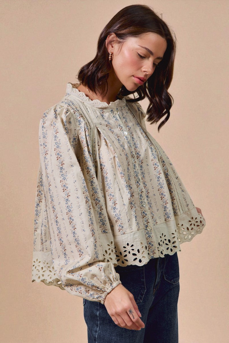 Woman wearing a floral blouse with cut-out sleeves against a beige background