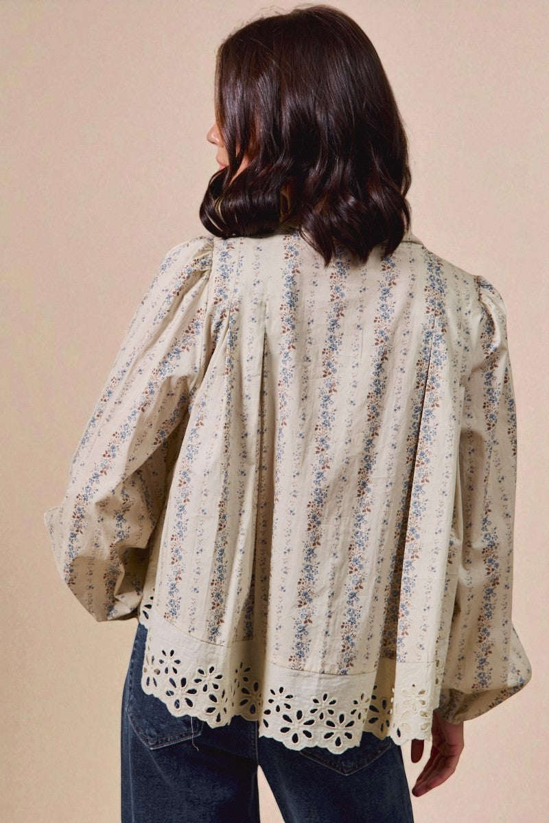 Woman wearing a floral blouse with long sleeves and cut-out details on a beige background