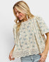 Woman wearing a floral blouse with lace details on a plain background