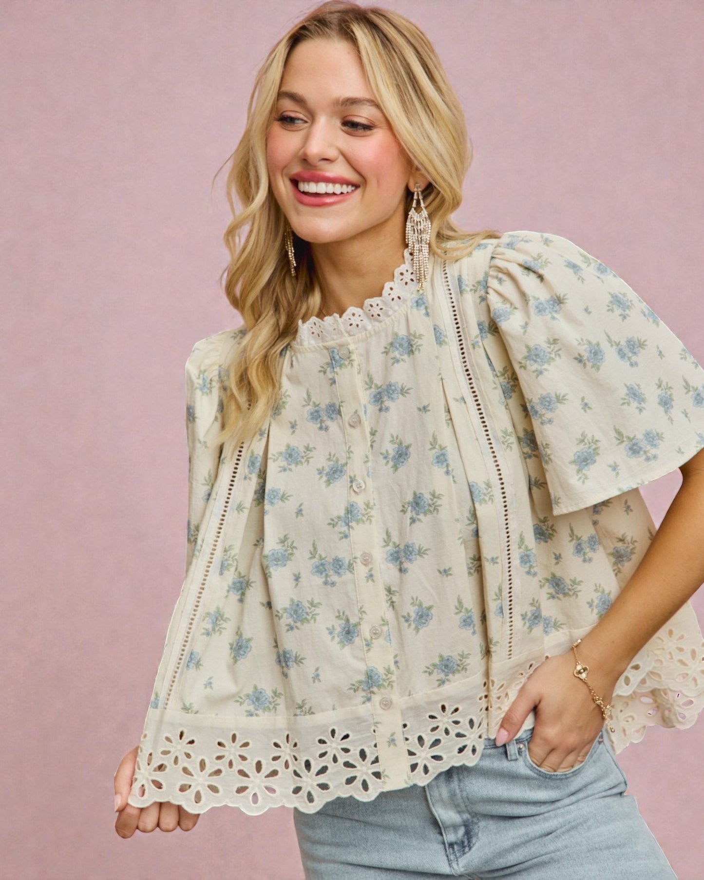 Woman wearing a floral blouse with lace details against a pink background