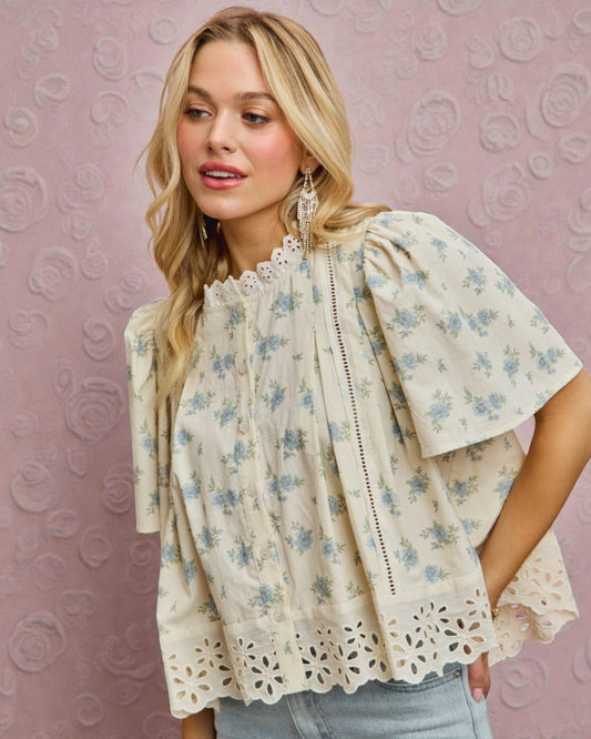 Woman wearing a floral blouse with lace details against a pink patterned background