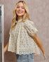 Woman wearing a floral blouse with a lace detail against a neutral background