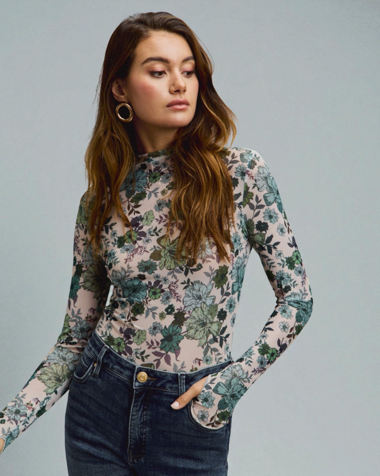 Woman wearing a floral long-sleeve top and jeans against a gray background