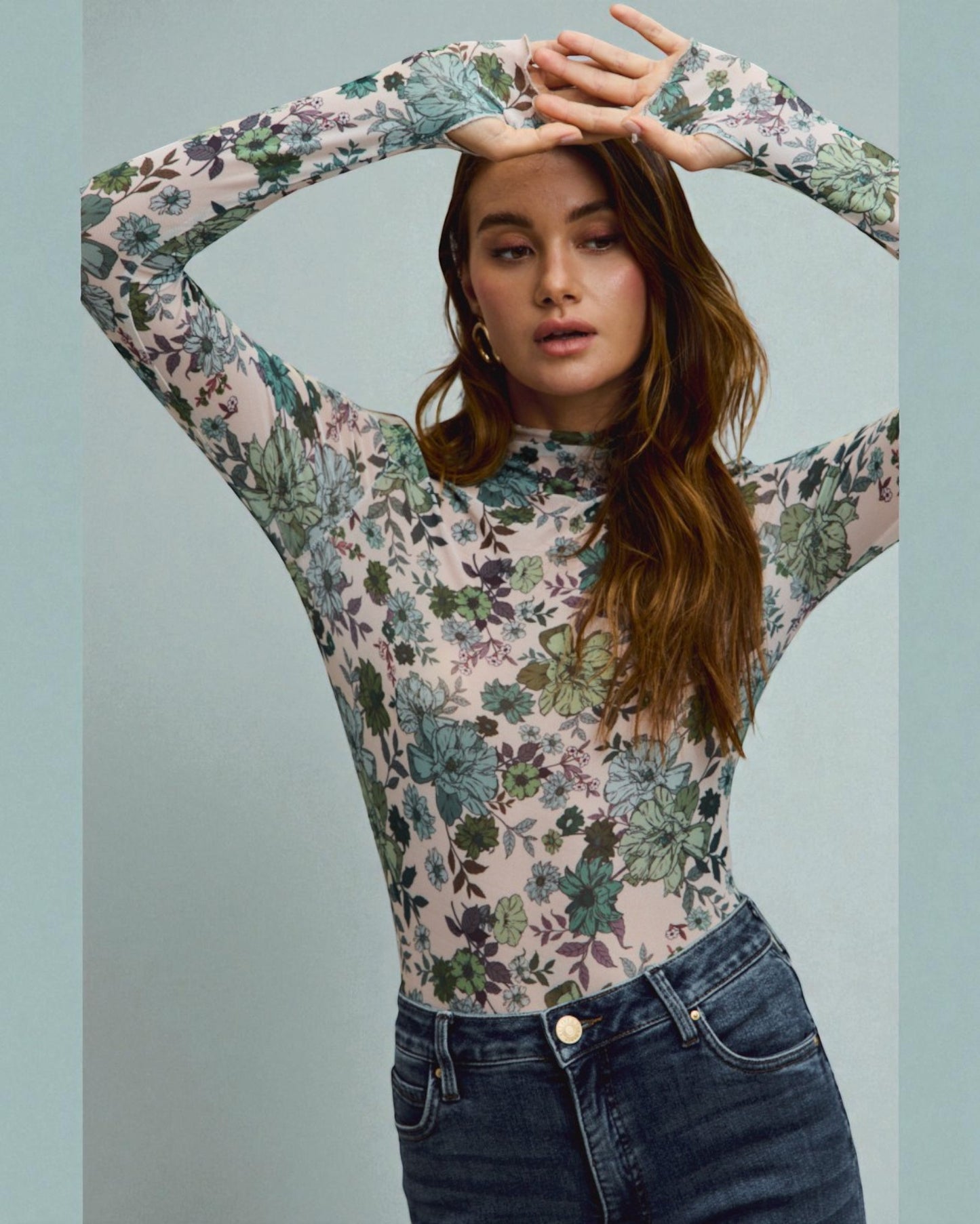 Woman wearing a floral long-sleeve top and jeans against a light blue background
