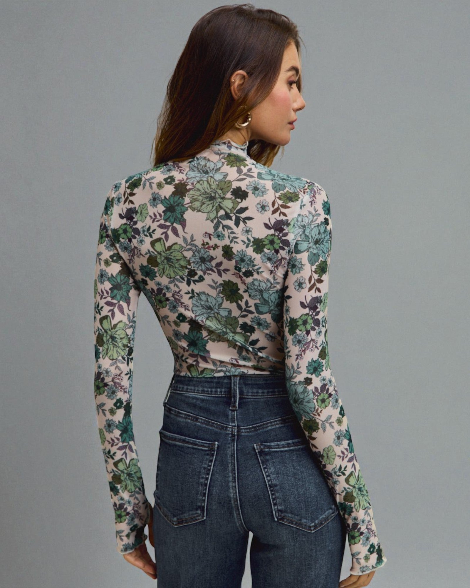 Woman wearing a floral long-sleeve top and jeans on a gray background