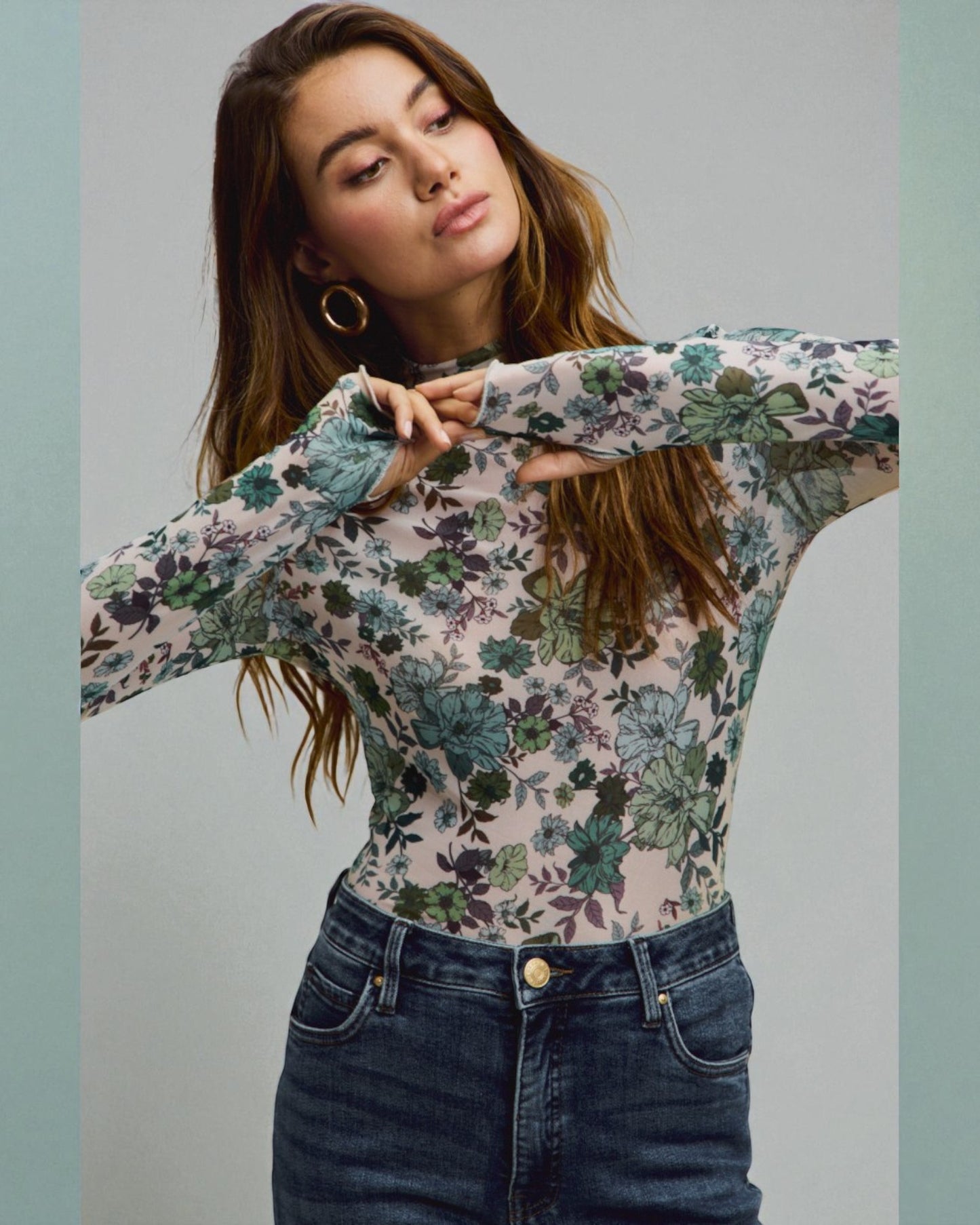 Woman wearing a floral long-sleeve top and jeans against a plain background