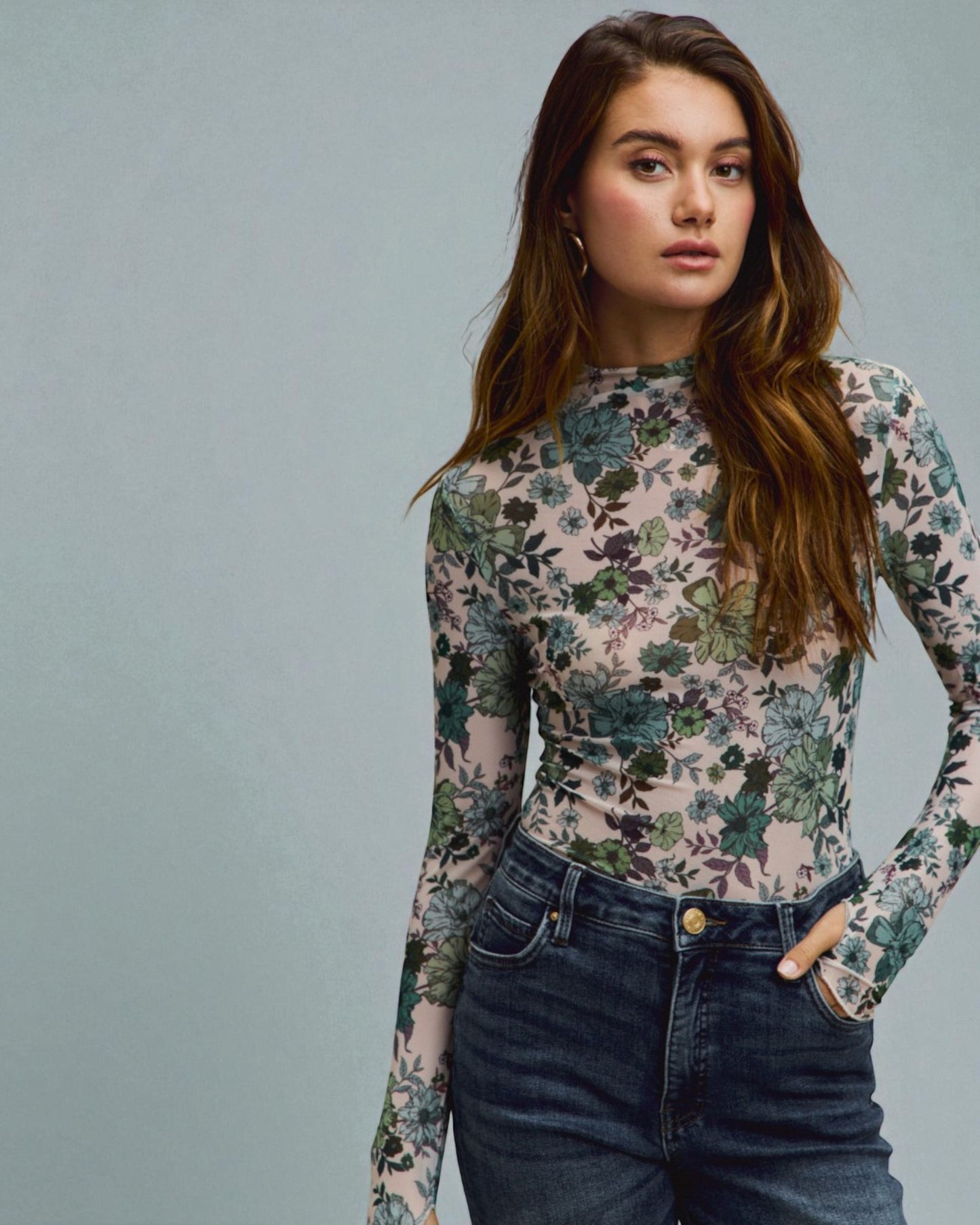 Woman wearing a floral long-sleeve top and jeans against a gray background