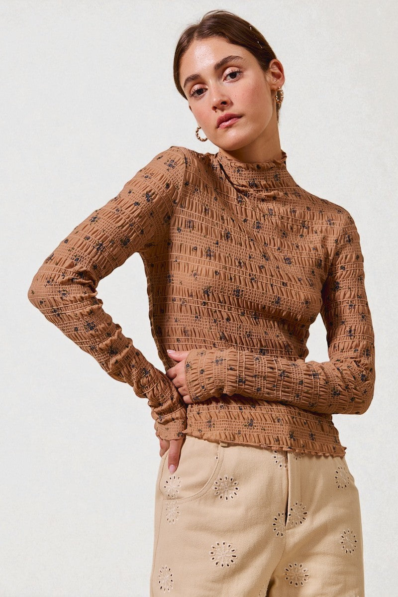 Woman wearing a brown patterned sweater and beige pants against a white background