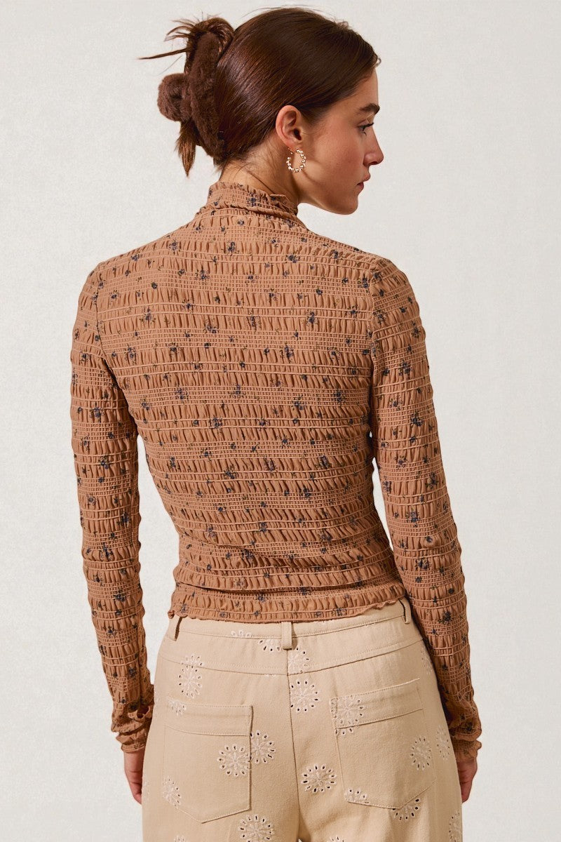 Woman wearing a patterned brown top and beige pants on a white background