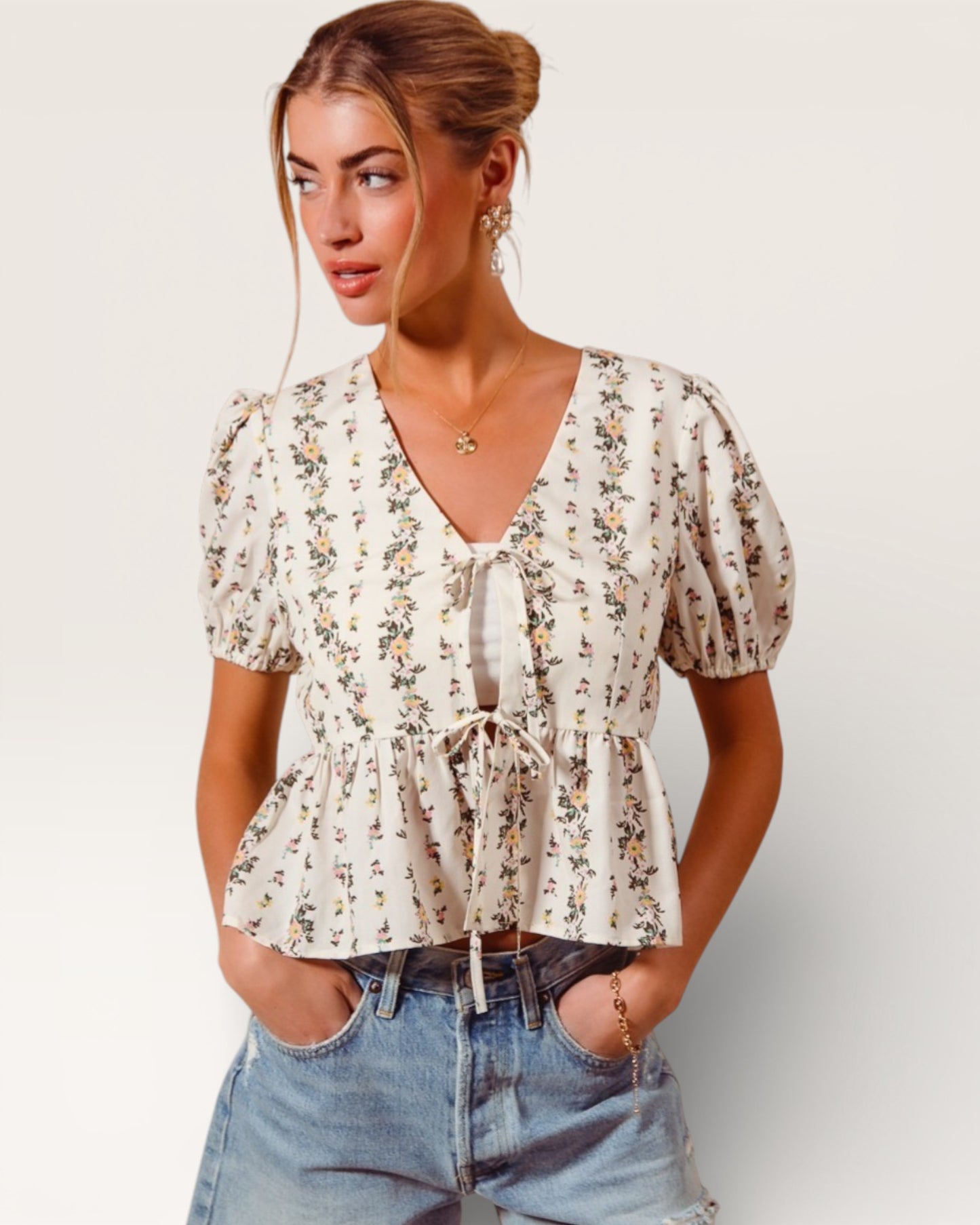 Woman wearing a floral blouse and denim shorts on a plain background