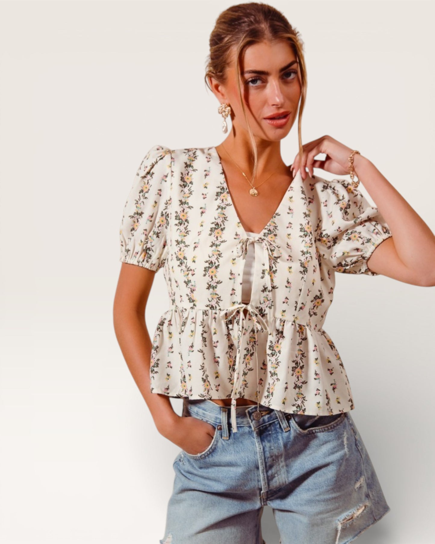 Woman wearing a floral blouse and denim shorts against a white background