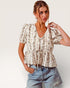 Woman wearing a floral blouse and denim shorts against a white background