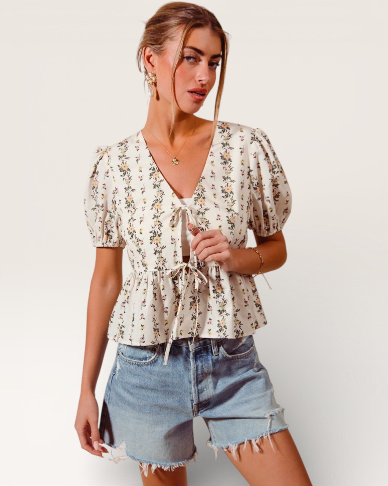 Woman wearing a floral blouse and denim shorts on a plain background