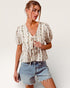 Woman wearing a floral blouse and denim shorts on a plain background