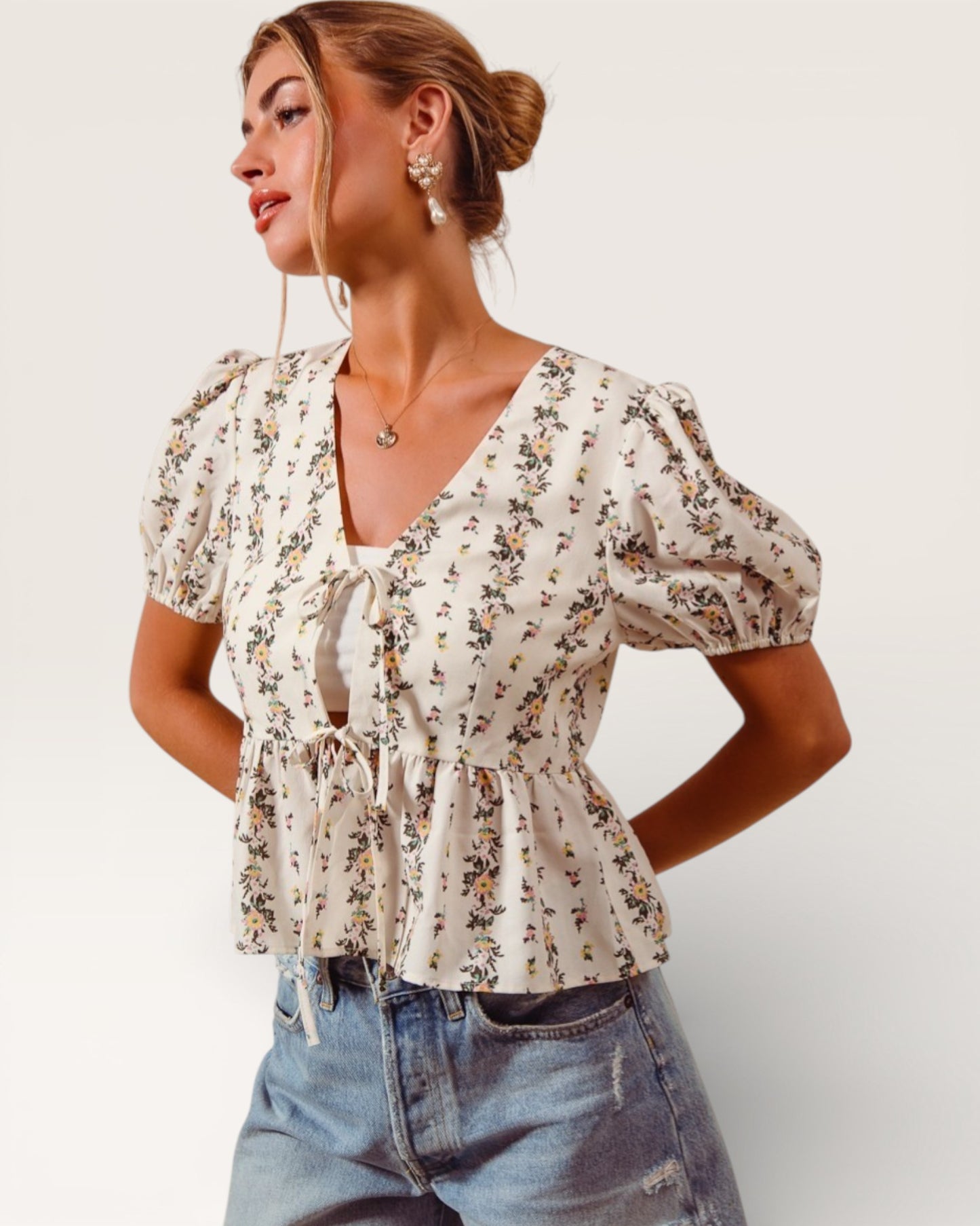 Woman wearing a floral blouse and denim jeans on a plain background