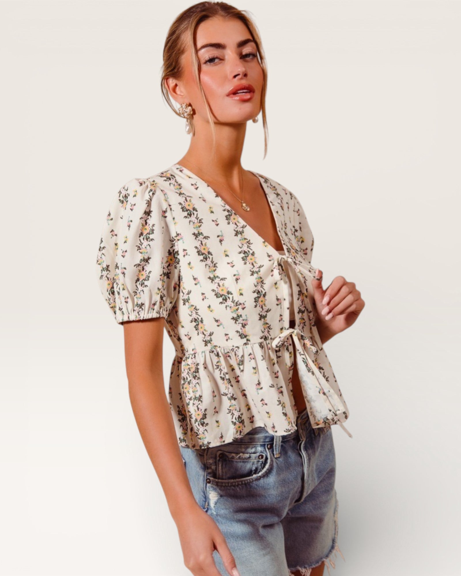 Woman wearing a floral blouse and denim shorts on a white background