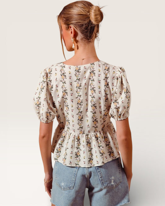 Woman wearing a floral blouse and denim shorts on a plain background