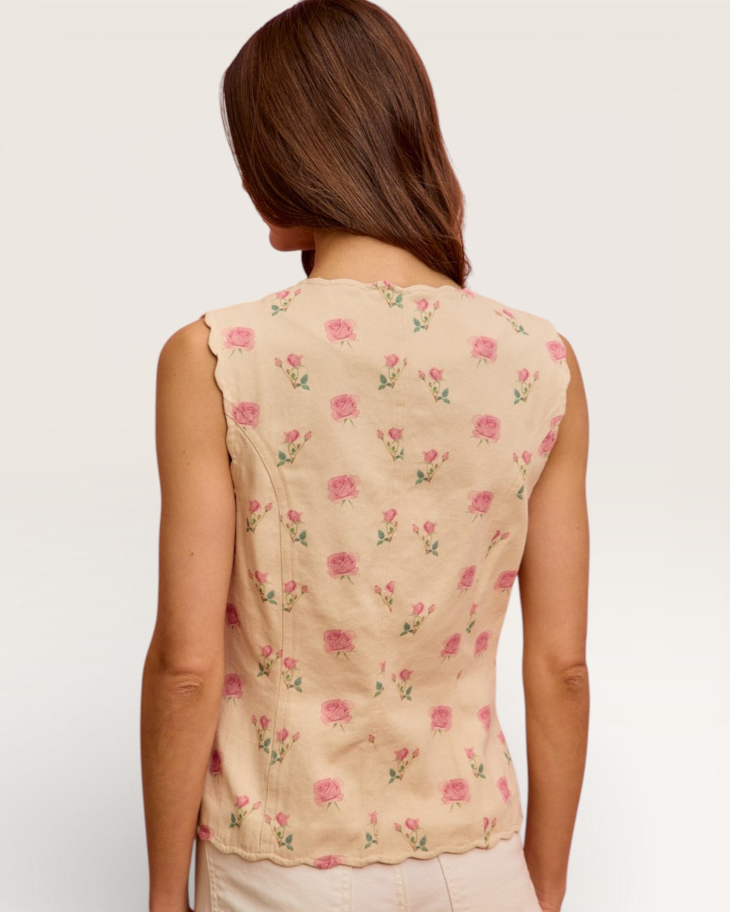 Woman wearing a beige sleeveless top with pink floral pattern on a plain background
