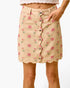 A beige mini skirt with a pink rose floral print, featuring a scalloped hem and a front button closure, shown on a model against a white background.