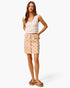 A woman modeling a sleeveless cream crochet top and a beige mini skirt with a pink floral print and scalloped hem, paired with brown platform sandals, against a plain white studio background.
